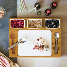 Serving board with white mixing plate, two metal scoops, and three ingredient boxes