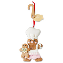White-hatted gingerbread chef ornament holding gingerbread kid; red hanging loop