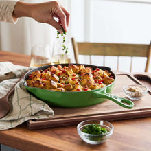 Green enameled cast-iron skillet with long handle, filled with roasted food on a table