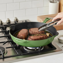 Green enameled cast-iron skillet on a stovetop, holding searing meat
