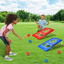 Children playing ball toss on red and blue boards with pom balls on grass