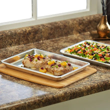 Aluminum 1/4-size baking sheet with roasted chicken on wooden board.