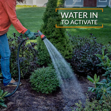 Weed preventer being watered in with a garden hose sprayer over shrubs