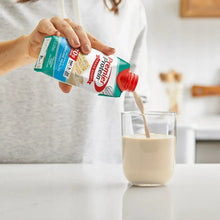 Protein shake carton, teal with red cap, pouring beige shake into drinking glass
