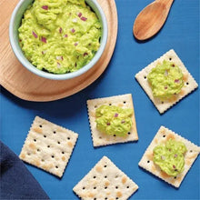 Saltine crackers topped with green spread and purple garnish, arranged on a plate