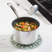 Silicone food lid, sage green base with molded handles on a stockpot