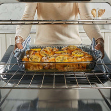 Tinted glass baking dish with blue lid on oven rack, roast topped with lemon slices