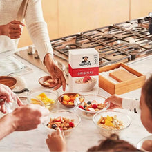 Quaker oats box on a breakfast table with bowls of fruit and cereal