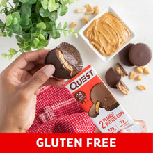 Peanut butter cup in hand with Quest package and several chocolate cups