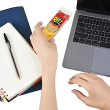 Hand holding RITZ cheese cracker sandwich box near laptop and notebook