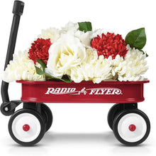 Red toy wagon filled with white and red flowers, with black wheels and handle