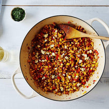 Skillet with mixed corn and vegetables, topped with diced peppers and seasoning
