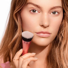 Makeup brush with soft white-and-black bristles held near face for base