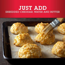 Baked cheddar biscuits in a tray, golden tops with green herb specks