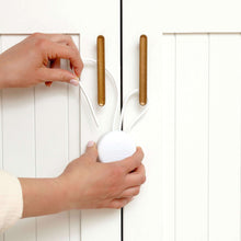 Hand installing a baby proof cabinet strap lock on white cabinet door