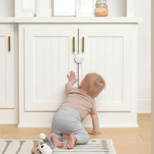 Baby proof cabinet strap locks on white cabinet doors with brown anchor bars