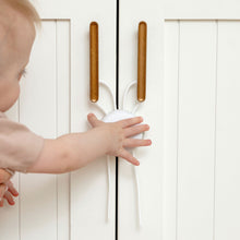 Child reaching toward installed cabinet strap lock with white round release and bars