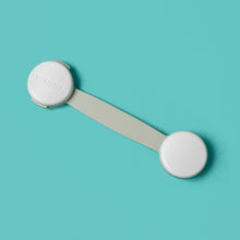 White safety latch strap with round adhesive covers, shown separated on flat surface