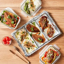 Foil-lined food tray with baked chicken, vegetables, and sauce