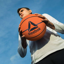 Orange Reebok basketball held in hands outdoors, textured grip and black seam lines