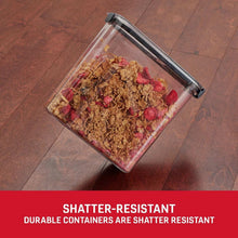 Clear cereal storage container with dark gray lid on floor, filled with granola
