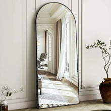 Arched full-length black-framed mirror reflecting a hallway view with tall windows and curtains.