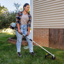 Gas string trimmer trimming grass beside a building wall and landscaping