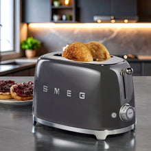 Dark gray SMEG 2-slice toaster with bread popping up in the slot openings