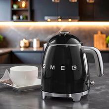 Black mini electric kettle with chrome handle and domed lid, SMEG letters on front.