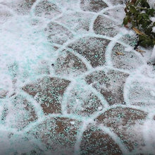 Ice melt granules spread on snowy brick patio near a gate and plants