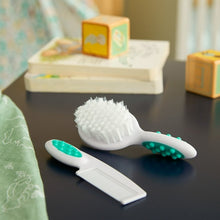 Baby brush and fine-tooth comb set on tabletop, white handles with teal pads