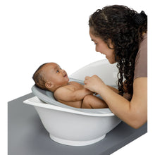 White baby bathtub with infant reclining while caregiver supports from the side