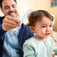 Infant with caregiver holding a white brush near the head