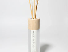 Reed diffuser bottle with light wood cap and white bottle, with reed stems