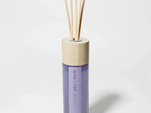 Reed diffuser bottle with light wood cap and purple glass base, with reed stems