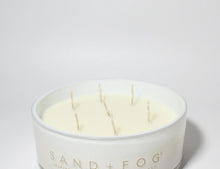 White scented candle in glass jar with four lit wicks and logo