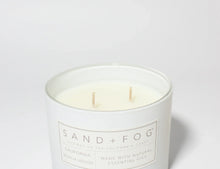 White scented candle in glass jar with two lit wicks and label