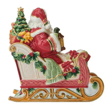 Holiday cookie jar with Santa sitting on sleigh, red suit and green tree, wrapped gifts.