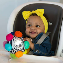 Sensory fabric ball toy with colorful bumpers and rattle ring held by a baby