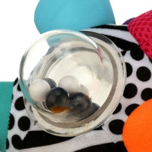 Close-up of clear rattle ring with white and dark beads on patterned fabric ball