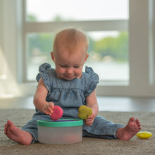 Baby playing with fruit fill-and-spill STEM toy, holding smiling fruit pieces