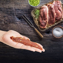 Duck jerky treat strips held in a hand on a dark wooden surface