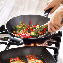 Nonstick wok with side handles, holding stir-fried vegetables and red peppers.