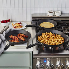 Three skillet set on stove, black nonstick pans with loop handles.