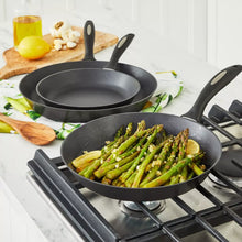 Nonstick French skillet with black handle on gas burner, part of a 3-pan set.