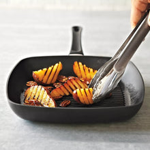 Square grill pan with ridged grate, black, with tongs lifting grilled fish