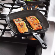 Square grill pan with ridged grate, black, on stovetop with grilled fillets