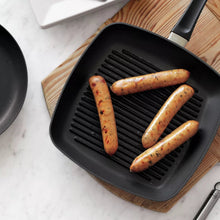Square grill pan with ridged insert, black, holding sliced sausages