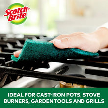 Green heavy-duty scour pad on stove grate, hand cleaning