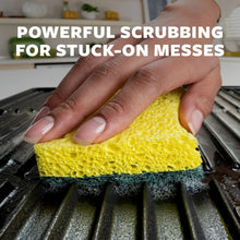 Hand holding yellow and green heavy duty scrub sponge on grill surface